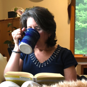 Julie drinking a cup of tea, while reading a book, and snuggling with her dog